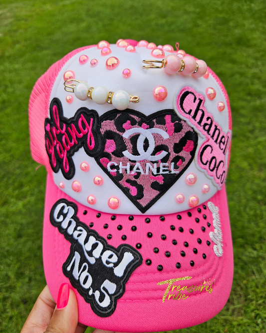 Pink cap with Cha*el elements and decorative elements on a grass background