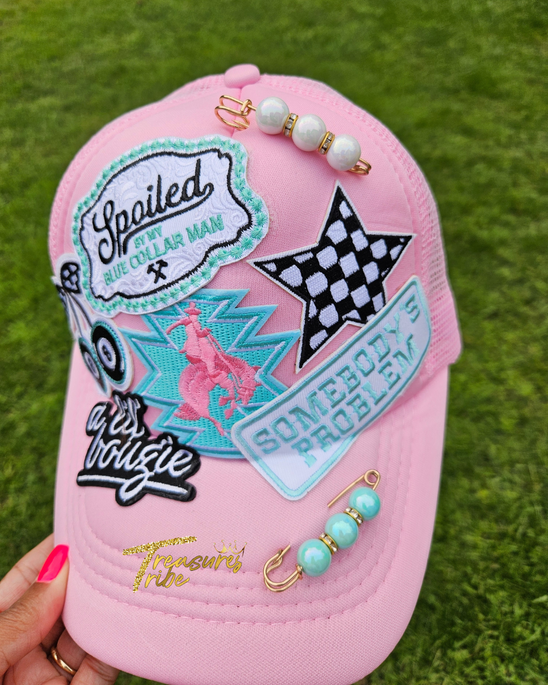 Pink cap with various patches and accessories on a grass background