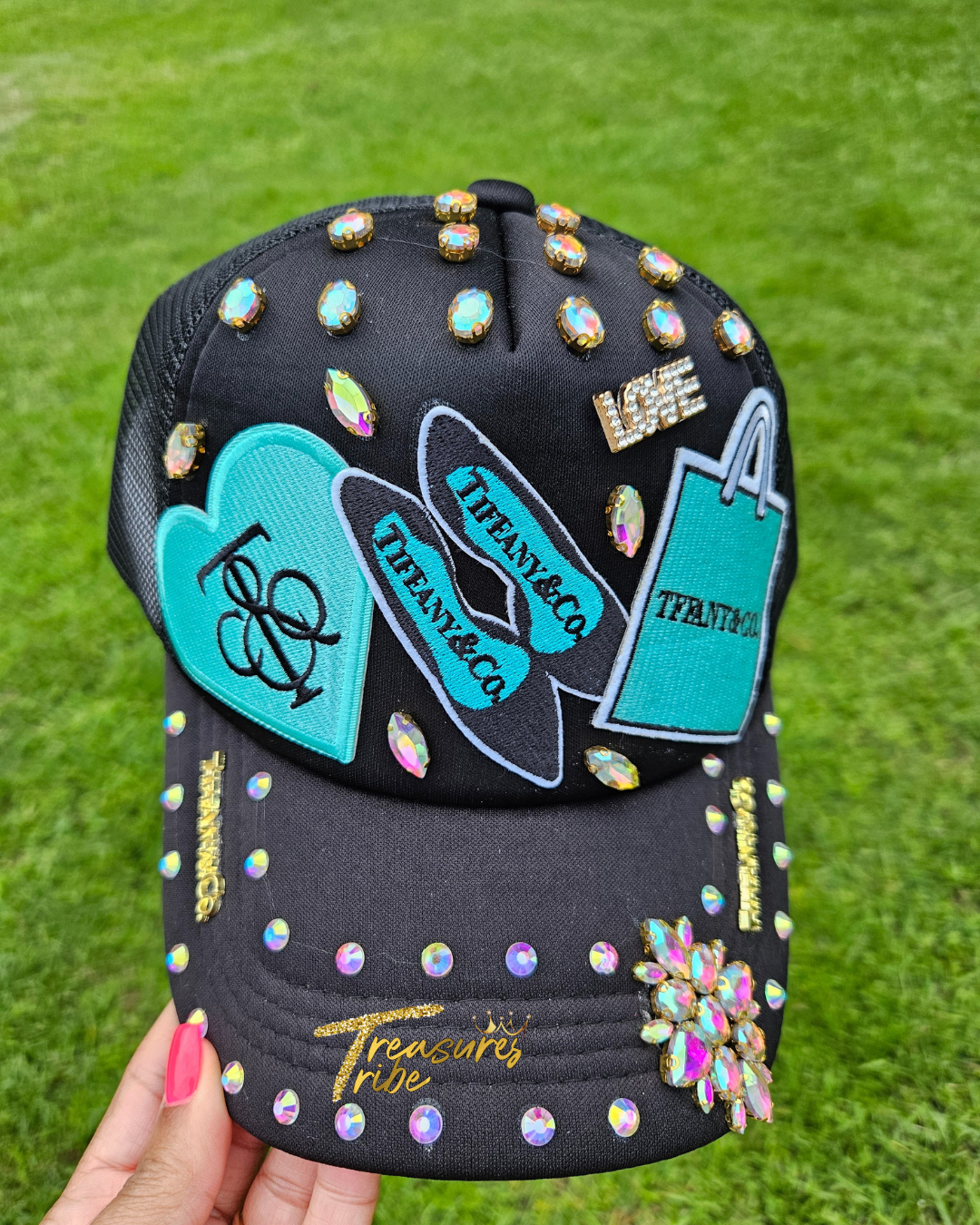 Decorative black cap with colorful embellishments held against a grass background